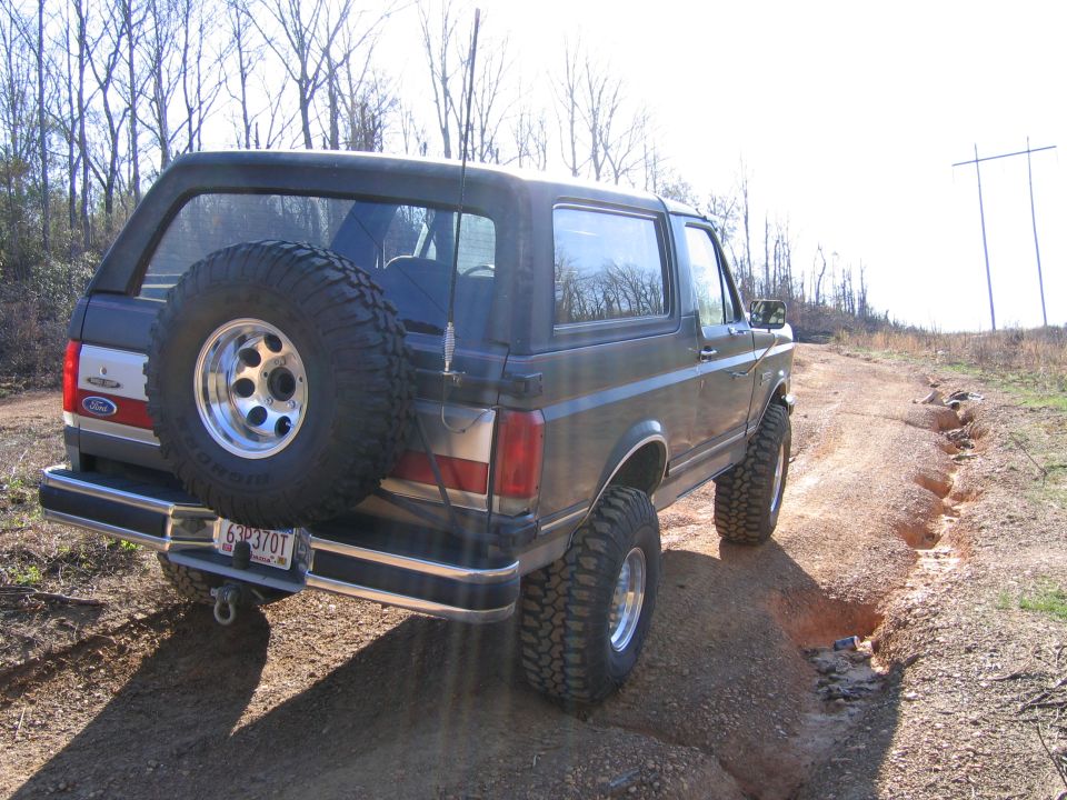 1989 Ford Bronco with spare tire on rear, driving on a dirt trail with ruts
