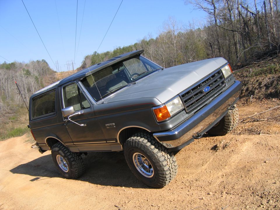 1989 Ford Bronco with lifted suspension and off-road tires driving on a dirt trail