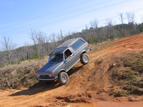 1989 Ford Bronco - This SUV, likely a 1987 Ford Bronco, navigates a challenging off-road terrain with muddy tracks.