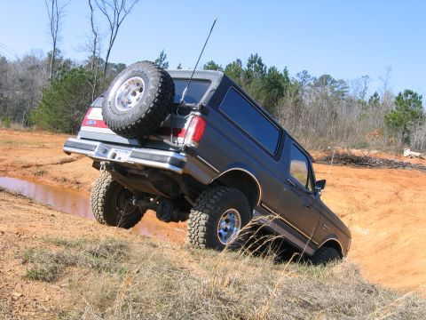 1989 Ford Bronco - This lifted Ford Bronco navigates a challenging off-road course, kicking up mud as it climbs.