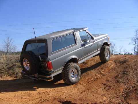 1989 Ford Bronco - 1989 Ford Bronco tackling an offroad trail with a clear blue sky overhead.