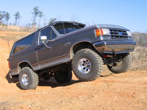 1989 Ford Bronco - This lifted Ford Bronco is navigating a dirt trail with its front wheels elevated.