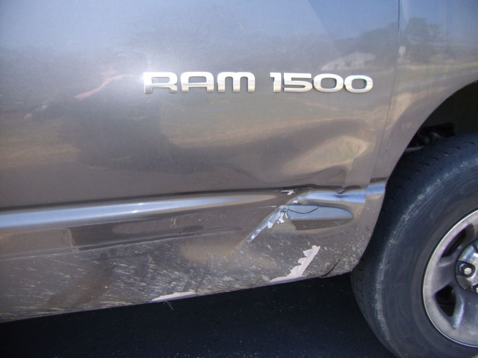 Dodge Ram 1500 badge on dented side panel, showing damage near the rear wheel well