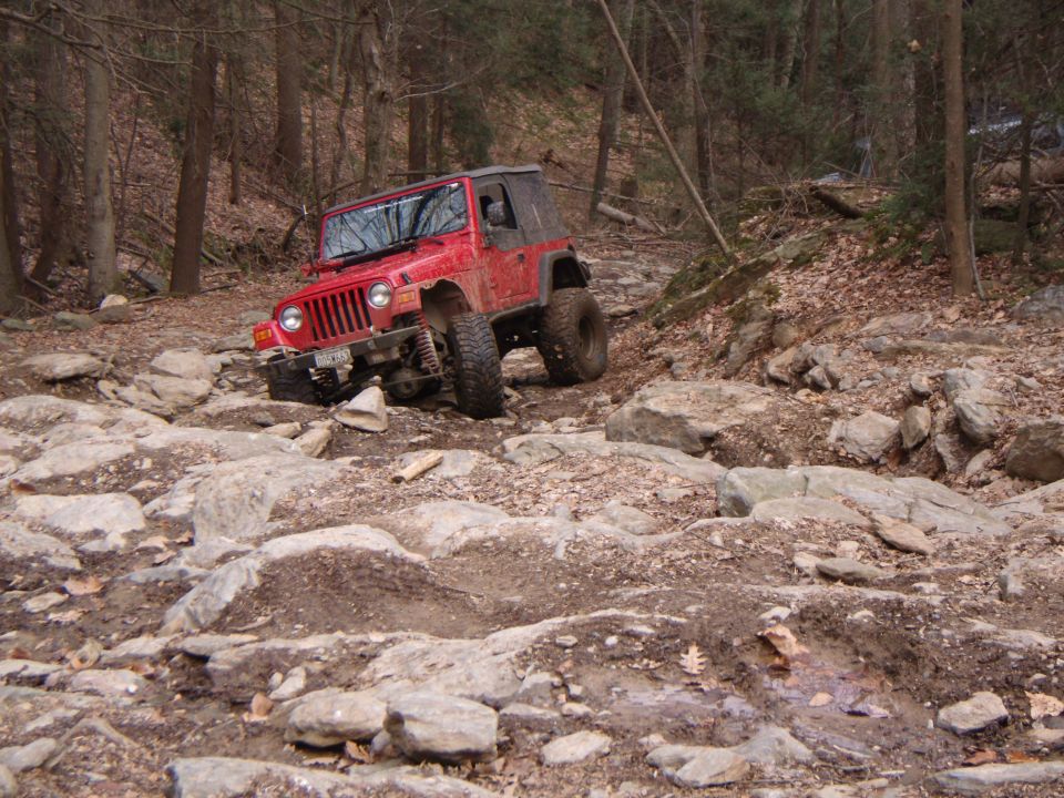Red 2003 Jeep Wrangler navigating a rocky off-road trail
