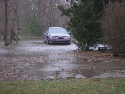 1997 Ford Taurus - A purple 1997 Ford Taurus sits partially submerged in floodwaters, surrounded by trees and debris.
