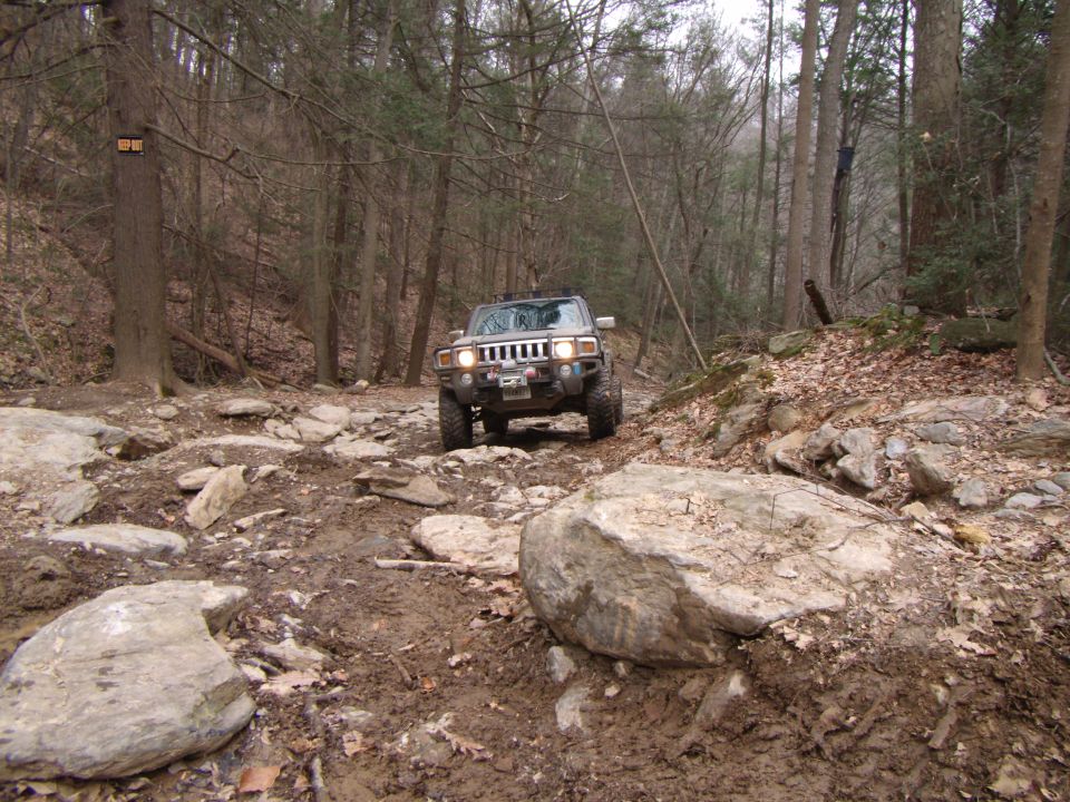 Hummer H3 driving on a muddy, rocky trail through a forest