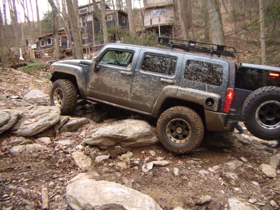 Mud-covered Hummer H3 navigating a rocky, wooded trail