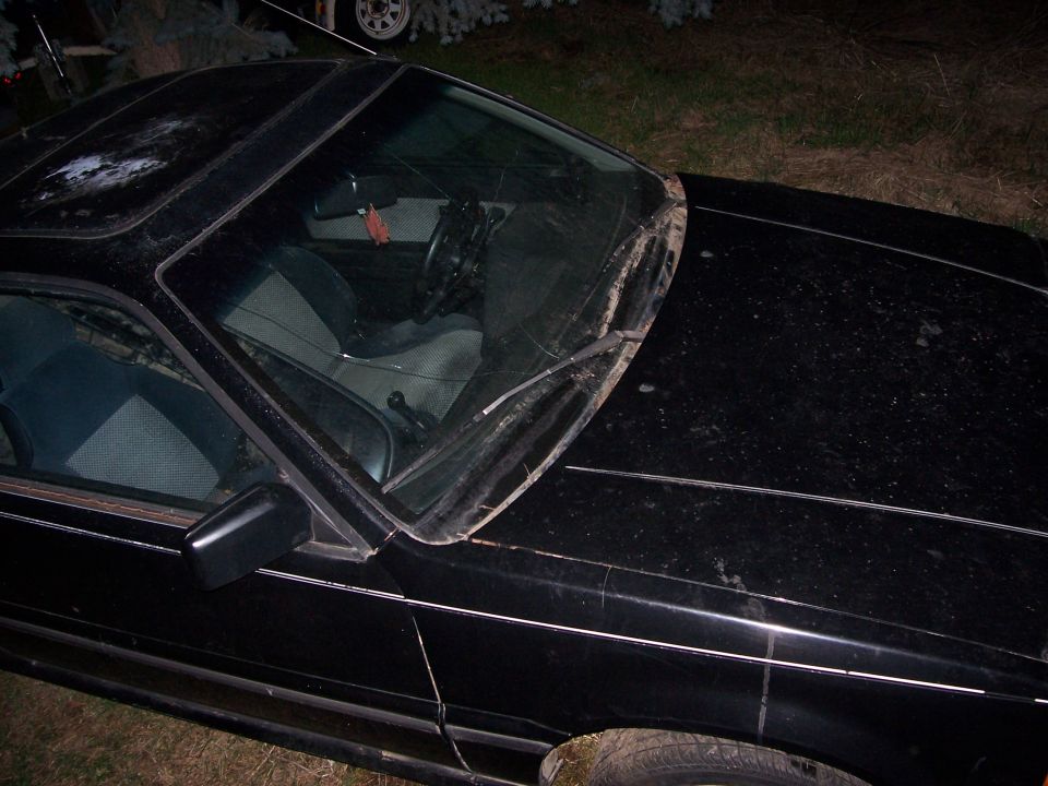 Dusty black coupe at night, front-corner view with windshield and gray interior visible