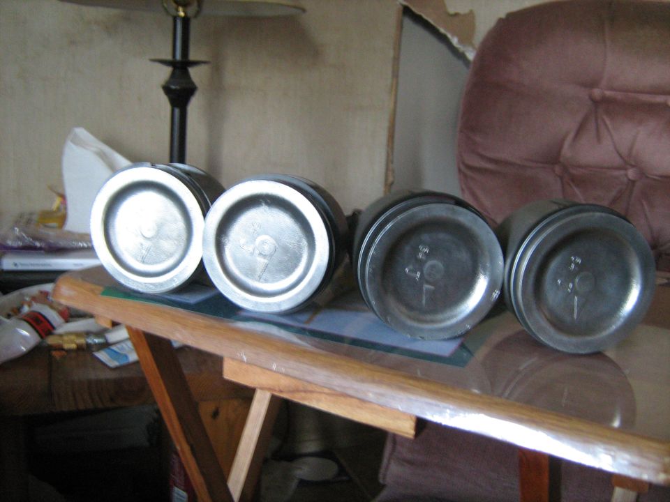 Four metal pistons on a table, two on the left with a '9' marking, two on the right with '34 7' markings
