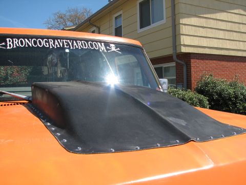 1979 Ford Bronco - A black cowl induction hood is bolted onto the orange hood of a truck, with a website sticker visible on the windshield.