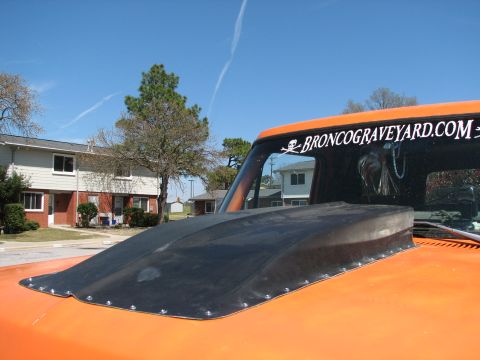 1979 Ford Bronco - A close-up of an orange truck's hood a black cowl induction scoop and a website sticker on the windshield.
