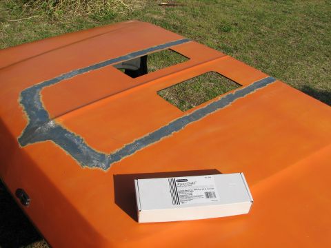 1979 Ford Bronco - A car hood, possibly modified, sits outdoors with a box of parts on its surface.