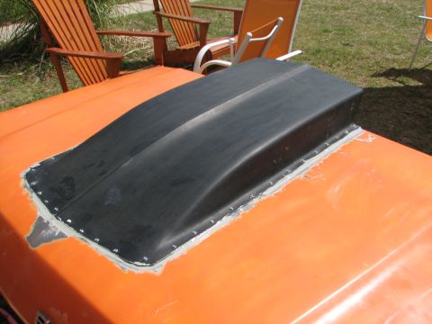 1979 Ford Bronco - Aftermarket cowl hood scoop installed on an orange vehicle's hood with visible rivets and sealant.