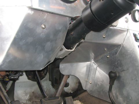 1990 Ford Bronco - Close-up inside a fabricated cab showing the steering column, foot pedals, brake-release lever, and riveted aluminum panels.