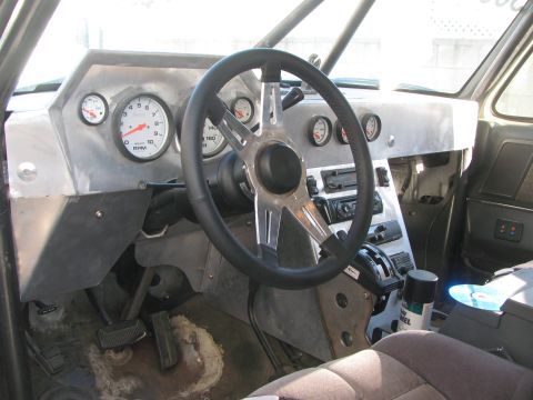 1990 Ford Bronco - Custom vehicle interior featuring a steering wheel, large tachometer and a row of round gauges set in a bare aluminum dashboard.