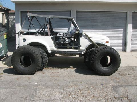 1987 Suzuki Samurai - A modified 1987 Suzuki Samurai with large tires sits parked in front of a garage.