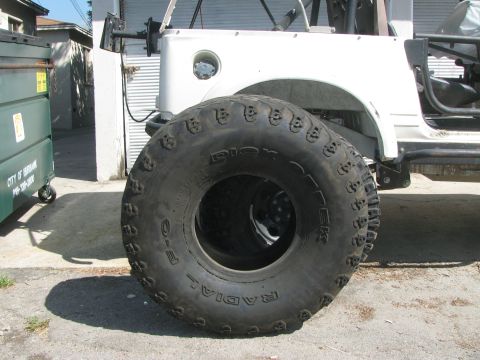 1987 Suzuki Samurai - A large, aggressive tire is mounted on a white off-road vehicle, obscuring much of the bodywork.