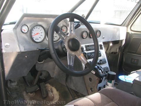1990 Ford Bronco - Custom vehicle interior with a steering wheel, tachometer and round gauges mounted in a bare aluminum dashboard.