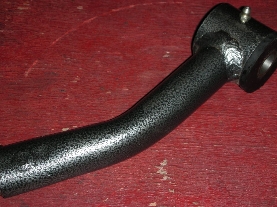 Black textured-coated curved metal tube fitting on a red workbench