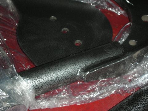 1998 Ford Crown Victoria - Detail of black textured-finish brackets and a tubular arm partially covered in plastic wrap on red bench.
