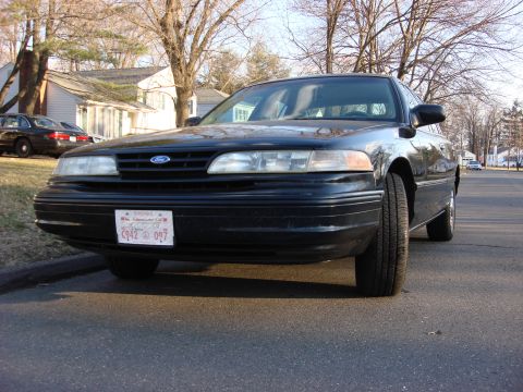 2003 Ford Crown Victoria - A black Ford Crown Victoria is parked on a residential street. Another car is visible in the background.