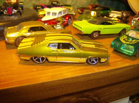 1970 Ford Ranchero - A collection of toy cars, including a gold 1970 Ford Ranchero, are displayed on a wooden surface.