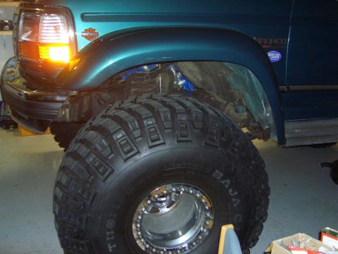 1996 Ford Bronco - A teal 1996 Ford Bronco XLT is shown with a massive off-road tire and chrome beadlock wheels, highlighting its modified suspension.
