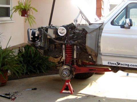 1996 Ford Bronco - A silver Ford SUV with its front end disassembled, front fender and headlight removed to expose the engine bay and front suspension. The fr…