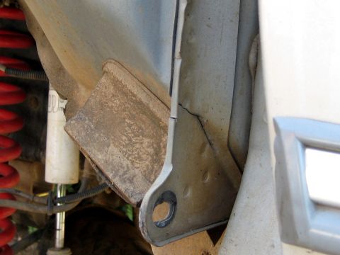 1996 Ford Bronco - Close-up of a rusty steel frame bracket and mounting area on the underside of a vehicle, showing a visible crack in the frame near a bolt h…