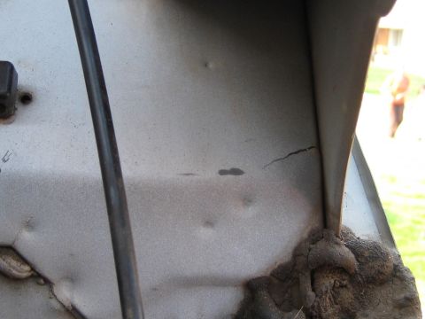 1996 Ford Bronco - Close-up of a silver-gray sheet metal panel showing a hairline crack near a welded seam, with rusty weld buildup at the bottom joint. A bla…