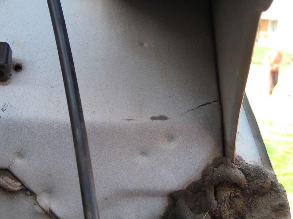 Cracked silver metal panel with rusty weld and vertical black rod