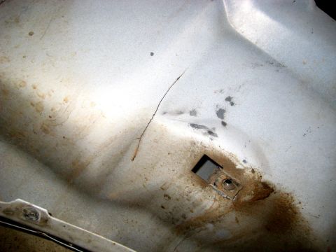 1996 Ford Bronco - Close-up of a silver-painted sheet-metal inner body panel showing a hairline crack running through the paint, dirt and rust-colored stainin…
