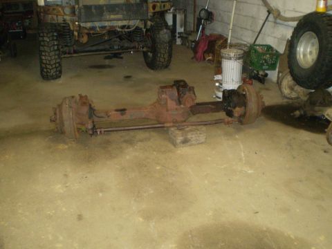 2005 Ford Excursion - A rusty front axle assembly is displayed on the floor of a garage, with a vehicle in the background.