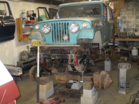 2005 Ford Excursion - Teal Jeep CJ-5 body on jack stands, front end visible, undergoing repairs in a garage.