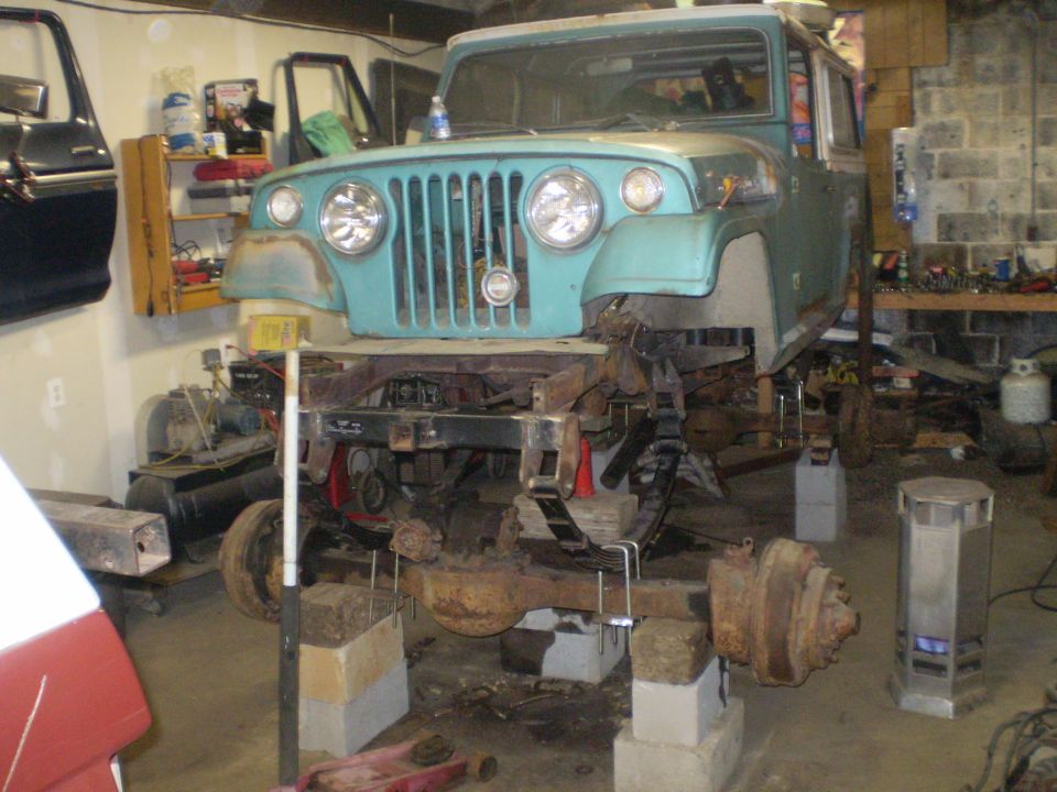 Teal Jeep CJ-5 body on jack stands, front end visible, undergoing repairs in a garage