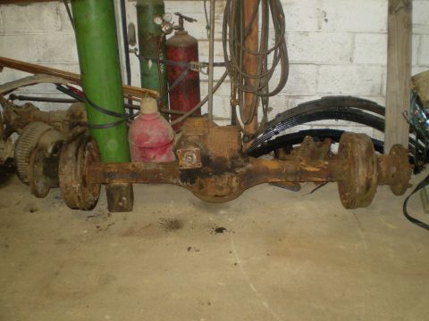 2005 Ford Excursion - A heavily rusted rear axle assembly, likely for a truck or SUV, sits on a concrete floor with various workshop items in the background.