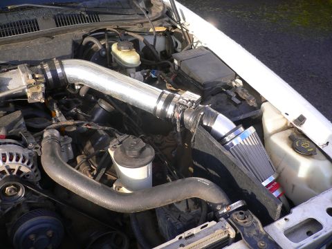 1999 Ford Crown Victoria - Aftermarket cold air intake installed in an engine bay, with visible brake fluid reservoir and alternator.