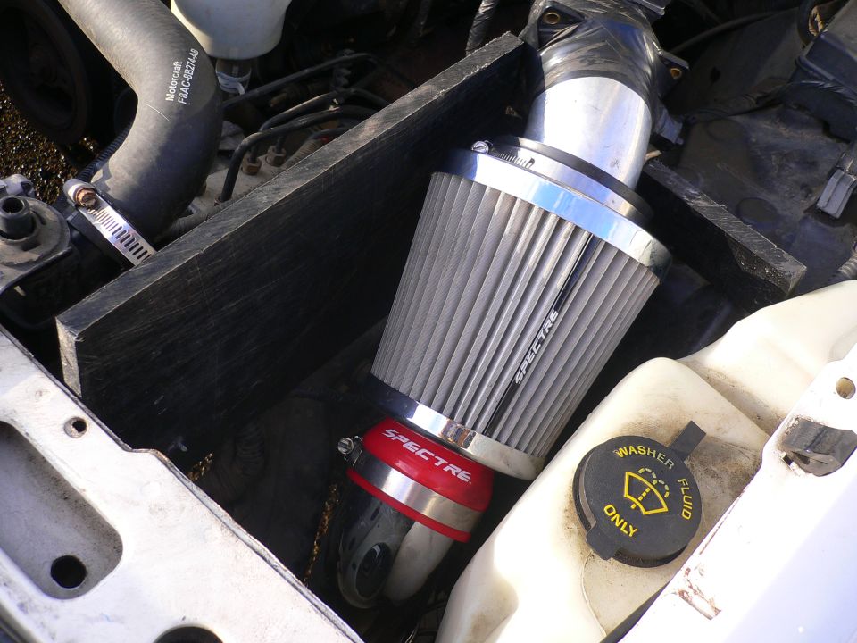 Close-up of a Spectre air filter and intake tube in an engine bay. Washer fluid cap visible
