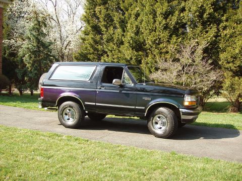1993 Ford Bronco - This 1993 Ford Bronco is parked outside on a paved driveway with trees in the background.