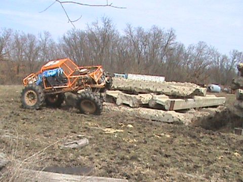 1973 Ford Bronco - An orange buggy sits on muddy terrain near a stack of concrete debris under a cloudy sky.