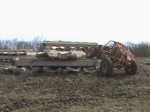 1973 Ford Bronco - An orange off-road buggy navigates a challenging obstacle course of concrete barriers.