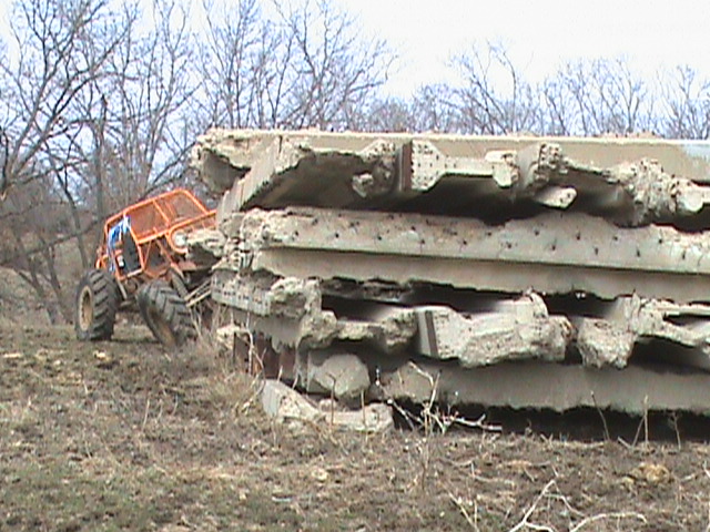 Orange off-road buggy with big tires next to a pile of broken concrete slabs
