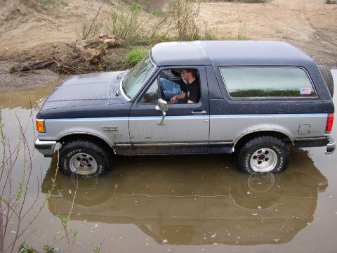 1989 Ford Bronco - This Ford Bronco is navigating through a water-filled, muddy terrain, with its reflection clearly visible.