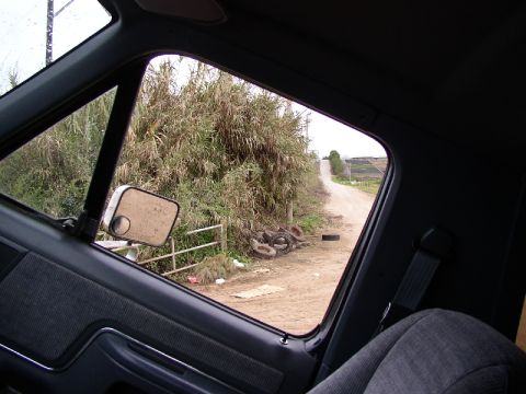 1989 Ford Bronco - View from inside a vehicle looking out the side window at a rural dirt road.