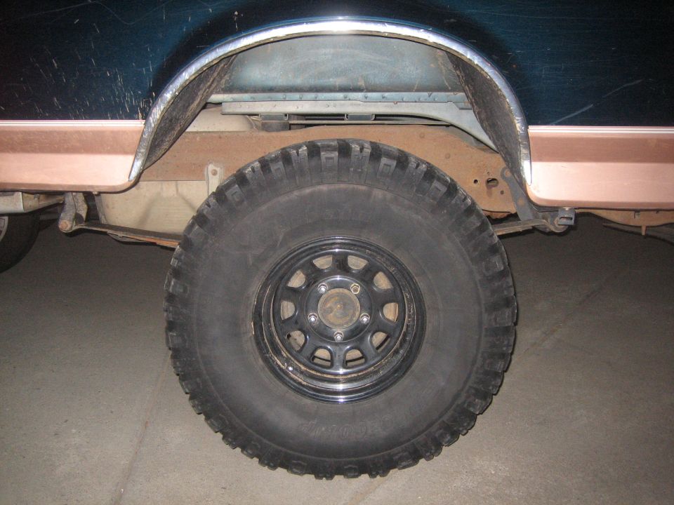 Rear wheel well and tire of a dark green vehicle with a brown stripe