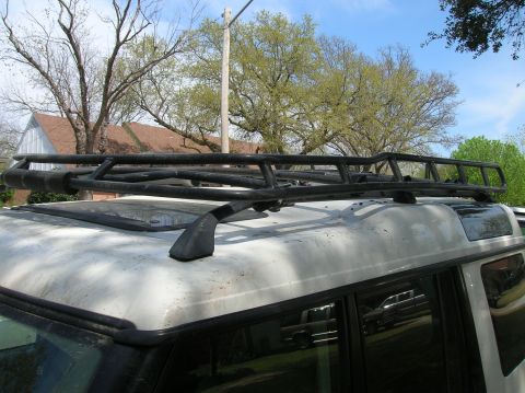 1999 Land Rover Discovery II - A white SUV with a custom black roof rack is shown from the side, with trees and a house in the background.