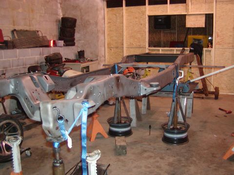 1991 Ford Bronco - The bare frame of a vehicle is supported by jack stands in a workshop environment.