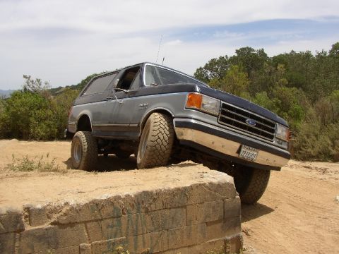 1989 Ford Bronco - This Ford Bronco is navigating a challenging off-road course, with one wheel significantly higher than the others.