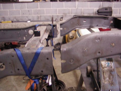 1991 Ford Bronco - Two gray metal vehicle frame sections are held up by jack stands and secured with blue straps.