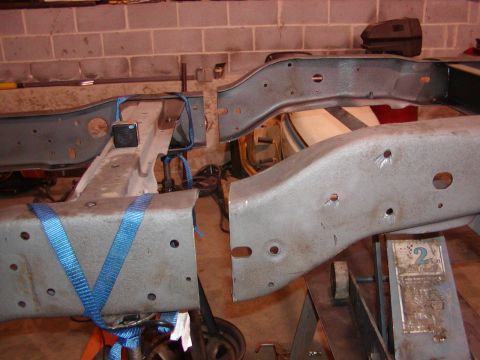 1991 Ford Bronco - Two sections of a vehicle frame are visible, one secured with blue straps, resting on stands in a workshop.